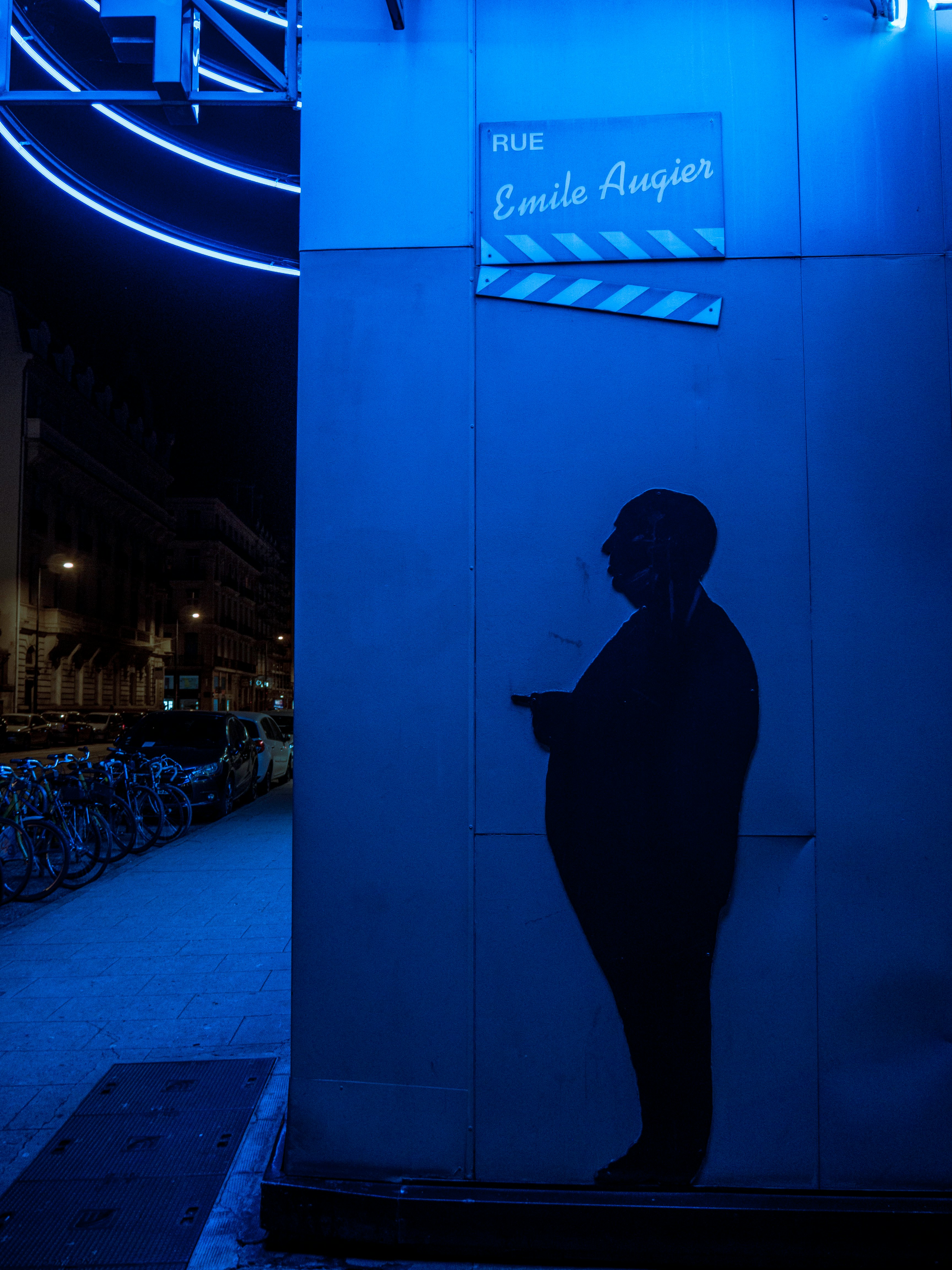 man in black coat standing in front of blue wall